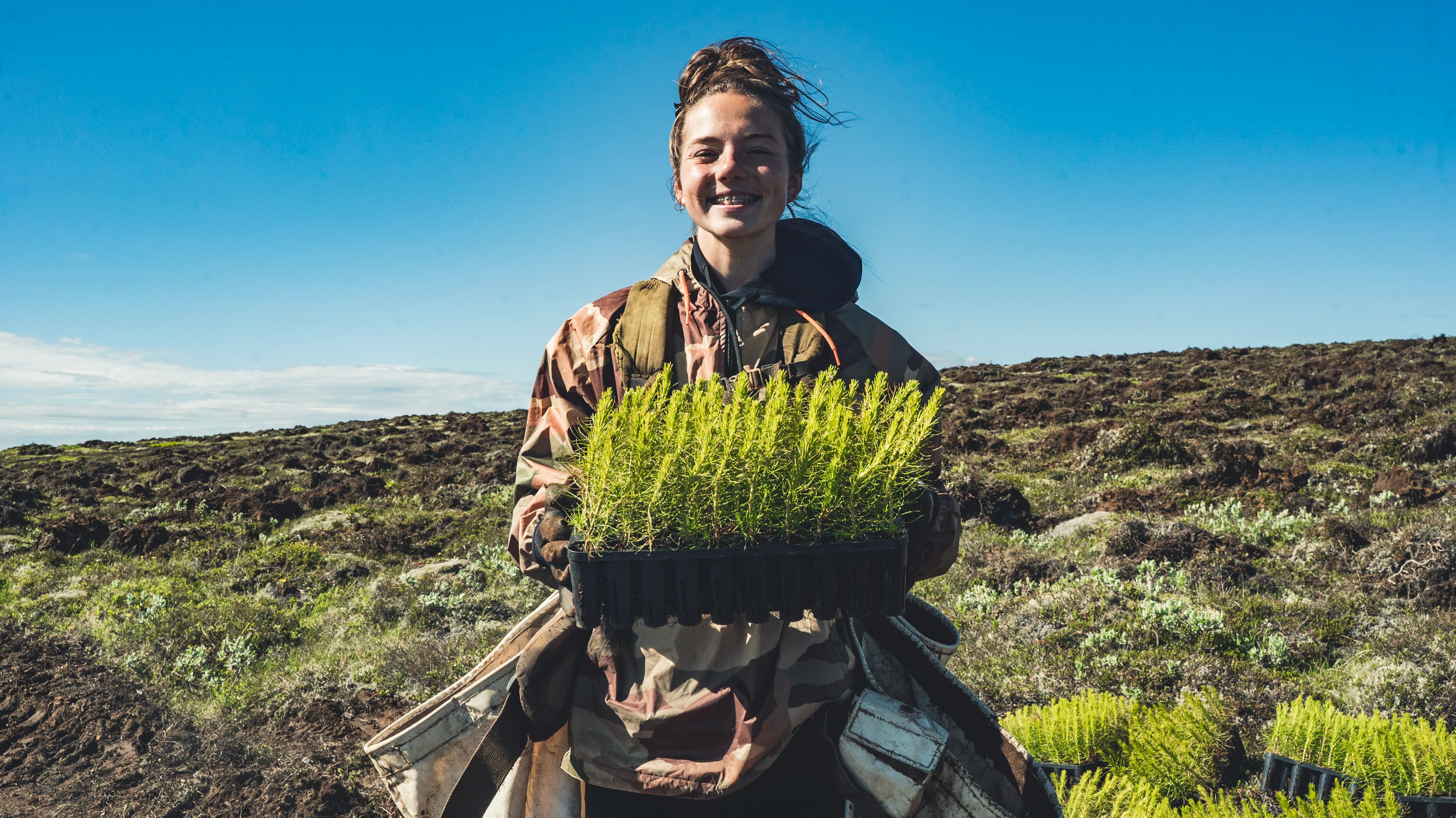 A smiling planter holding a tray of seedlings